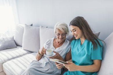 Happy patient is holding caregiver for a hand while spending time together. Elderly woman in nursing home and nurse. Aged elegant woman and tea time at nursing home